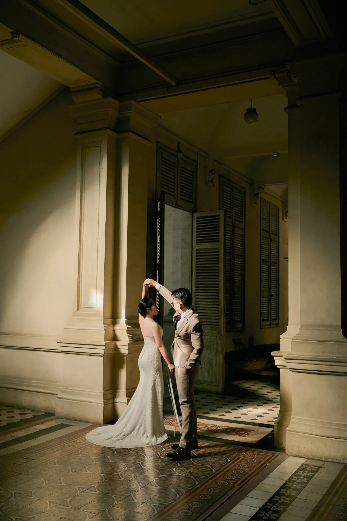 He turns her under his raised hand in a sunlit doorway of the old hall